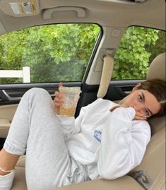 a woman sitting in the back seat of a car holding a drink and looking at the camera