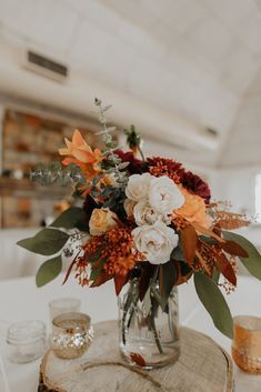 a vase filled with flowers sitting on top of a wooden table next to glasses and candles