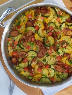 a large pan filled with lots of food on top of a wooden table next to utensils