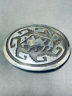 a metal belt buckle with an intricate design on the front and side, sitting on a gray surface