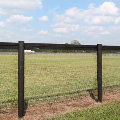 a black wire fence in the middle of a grassy field