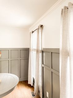 an empty room with gray paneling and white curtains on the windowsills is pictured in this image