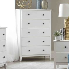 a white dresser sitting in a bedroom next to a lamp and bed with blue sheets on it