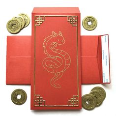 a red envelope with two gold coins and a chinese dragon design on the front, sitting next to it