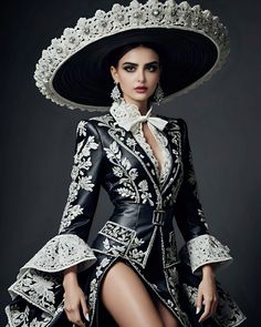 This stunning ensemble epitomizes the grace and heritage of traditional Charro fashion with a contemporary twist. The intricately embroidered black leather jacket, adorned with delicate white floral patterns, complements the dramatic flared sleeves and high-slit skirt. The oversized sombrero, with its detailed lace embellishments, crowns the look, exuding sophistication and timeless charm. This outfit is a testament to the enduring allure of classic Mexican design, reimagined for the modern fashionista.  #CharroElegance #ModernCharro #TraditionalFashion #CulturalHeritage #MexicanStyle #FashionFusion #ElegantFashion #TimelessDesign #HeritageInStyle #FashionArtistry #moodacouture #designer Mexican National Costume, Mexican Heritage Outfit, Charro Outfits For Women, Catrina Outfit, Mexican Outfit Ideas, Mexican Fashion Modern, Mariachi Dress, Mariachi Outfit