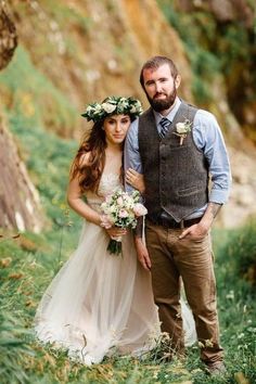 a man and woman standing next to each other in the grass with flowers on their head