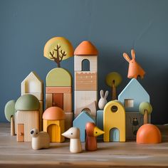 wooden toys are arranged on a table in front of a blue wall with trees and buildings