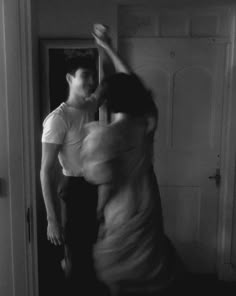 a man and woman are dancing in the hallway together, black and white photograph by an open door