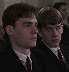 two young men sitting next to each other in suits and ties, looking off into the distance