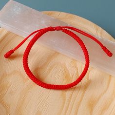 a red string bracelet sitting on top of a piece of wood next to a plastic container