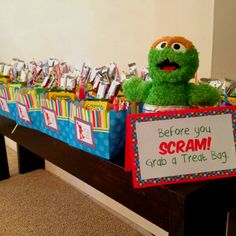 there is a table with some candy and a sesame the monster sign on it that says, before you scream grab a treat bag