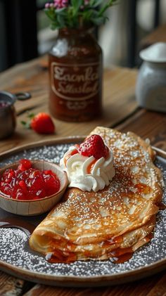 pancakes with whipped cream and strawberries are on a plate next to a bowl of jam