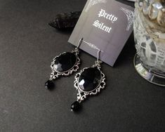 A pair of stylish gothic earrings with black faceted glass stones set in a beautiful ornamental frame. Black teardrop beads complete the elegant look. The earrings have a pleasant weight (see below) and come with stainless steel leverbacks. The frame is made of silver-plated metal alloy. The folding closure makes them easy to handle and sits very securely. Size: Glass cabochons: 18 x 25 mm Frame: 28x40mm Total length (including brisures): 72 mm Weight: 9 grams per earring If you would like to purchase a larger quantity than available, please message me. The item comes nicely and lovingly packaged. I am available for any questions! Gothic Drop Earrings For Formal Occasions, Victorian Black Earrings For Party, Silver Gothic Earrings For Formal Occasions, Gothic Formal Earrings For Pierced Ears, Ornamental Frame, Gothic Earrings, Black Stones, Teardrop Beads, Snap Fasteners