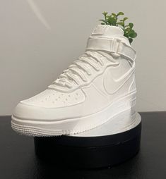 a pair of white nike sneakers on top of a black platform with a plant growing out of it