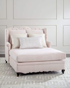 a pink chair with pillows on top of it in front of a white wall and carpet