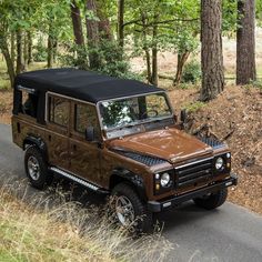 a brown jeep parked on the side of a road in front of some tall trees