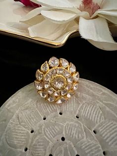 a gold ring sitting on top of a white table next to a flower and a mirror