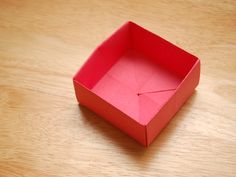 an empty red box sitting on top of a wooden table next to a piece of paper