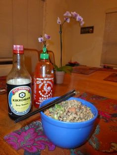 a blue bowl filled with food next to two bottles of ketchup and chopsticks