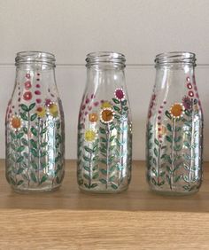 three glass jars with flowers painted on them sitting on a shelf next to a wall