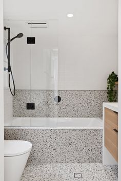 a white bathroom with black and white speckles on the floor, tub, toilet and shower