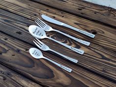 three spoons and two forks with words on them sitting next to each other in front of a wooden table