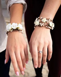 two people wearing bracelets with flowers on their wrist and one holding the other's hand