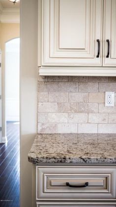 a kitchen with white cabinets and marble counter tops