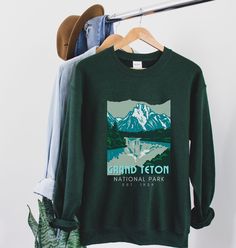 Grand Tetons Sweatshirt | Retro WPA Art Poster Graphic Printed on a classic unisex Gildan cotton sweatshirt. Colors: Forest Green *50% Cotton 50% Polyester *Medium-heavy fabric * Loose fit *Runs pretty true to size, slightly larger ♥♥SIZING♥♥ ♥Modern Unisex Fit. Women may want to size down if you prefer a more fitted look. Men may want to size up if you want a looser fitting shirt. SHIPPING TIMES ♥It takes us about 1-7 days to create your item. Designs are handmade and printed as soon as you pla National Park Sweatshirt, Winter Park Colorado, Shirt Printer, Camp Shirts, National Park Gifts, National Park Shirt, Vail Colorado, Mountain Shirt, Hiking Shirts