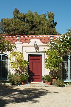 a house with red doors and windows surrounded by greenery on both sides of the front door