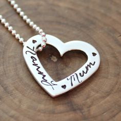 a heart shaped necklace with the word mama engraved on it's side, sitting on top of a piece of wood