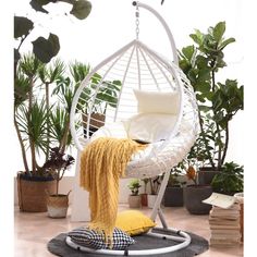 a hammock chair with a yellow throw pillow and some plants in the background