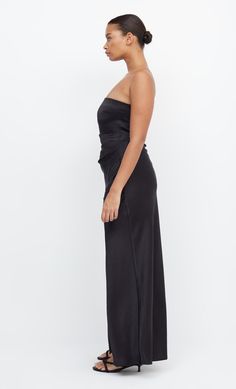 a woman in a black strapless dress is standing and looking off to the side