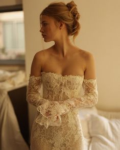 a woman in a white dress is standing near a bed and looking off to the side