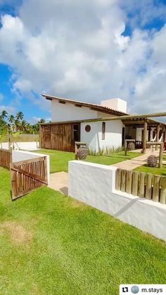 a house that is on the grass with a fence and some bushes in front of it