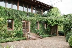 a house covered in vines and plants next to a brick walkway with steps leading up to the front door