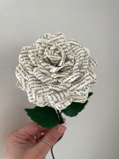 a hand holding a paper rose made out of old book pages with the word love written on it