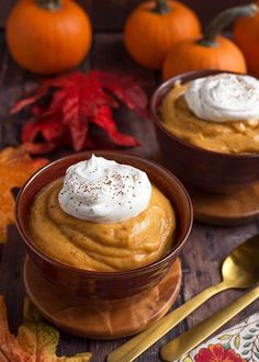 two small bowls filled with pumpkin pudding on top of a wooden table next to autumn leaves