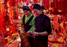 two women standing in front of red lanterns with chinese writing on them and one holding a book