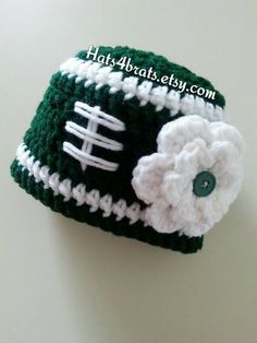 a crocheted hat with a football on it and flower in the center, sitting on a table