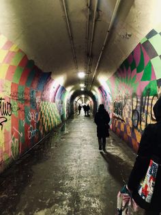 people are walking through a colorful tunnel with graffiti on the walls and floor, while another person is standing in front of them