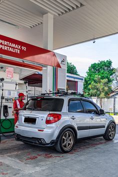 a silver car is parked in front of a gas station with an attendant at the pump