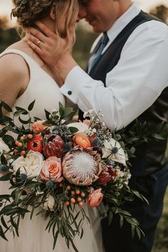 a bride and groom embracing each other in front of the camera with their wedding bouquet