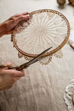 two hands are holding a piece of lace and scissors on a table with doily