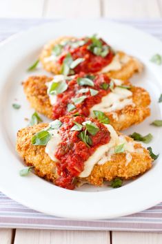 two chicken parmesan patties on a white plate with red sauce and basil