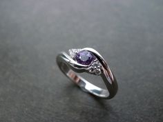 a close up of a ring with a purple and white diamond in the center on a black surface