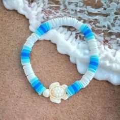 a blue and white beaded bracelet with a turtle on it sitting next to the ocean