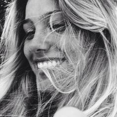 a black and white photo of a woman with her hair blowing in the wind, smiling