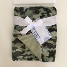 a green camouflage blanket with white ribbon tied around the edge and tag attached to it