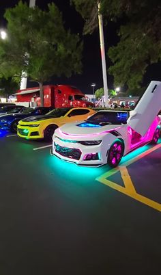 several cars are parked in a parking lot at night with colorful lights on the sides